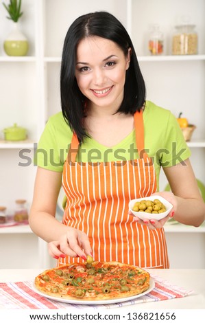 Girl housewife with delicious pizza on kitchen background
