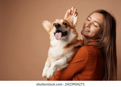 Girl hugging Pembroke Welsh Corgi on a beige clean background in the studio, love for animals - Powered by Shutterstock