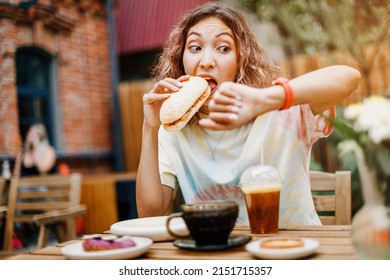 A girl in a hurry bites a burger on the run in a fast food cafe and looks at the smart watch. Late for a meeting and punctuality and digestive problems