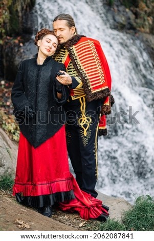
Girl and Hussar are hugging each other at a waterfall in autumn