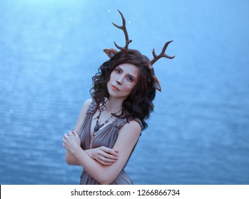 Girl In The Image Of A Faun, Costume And Make-up Of A Deer, A Fantastic Character Of The Spirit Of Forest In Brown Dress, Portrait Photo Of A Sad Lady On Background Of Magical Lake, Blue Cool Shades