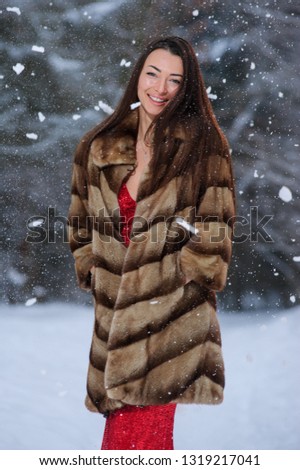 A girl in a image of a queen poses in a snow-covered winter forest. Long red dress, bouquet of fruits, red apples.