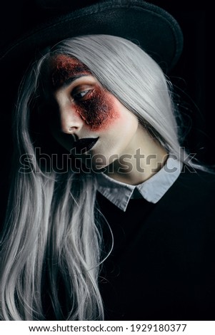 a girl in the image of a witch on Halloween with ash-colored hair, black lips and a burn on her face