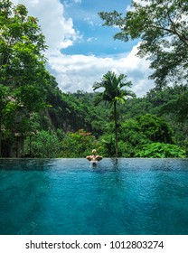 Girl in infinity pool towards jungle with palmtrees