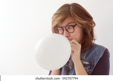 Girl inflates a balloon getting ready for a party. She's afraid of the explosion, so screwed up eyes