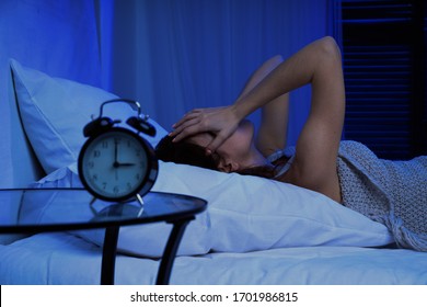 Girl with insomnia lying on bed next to alarm clock at night
