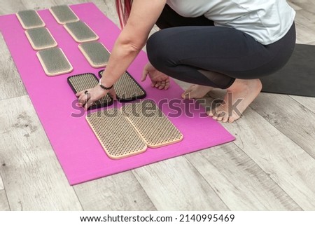 A girl instructor lays out wooden yoga boards with nails on a pink sports mat for yoga and meditation. Sadhu board with nails restores strength after training.