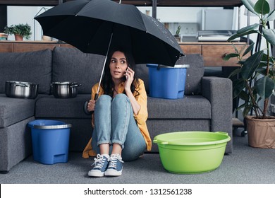 Girl in jeans sitting in living room with umbrella and talking on smartphone