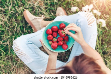 Girl in jeans sitting in summer grass and holding a plate of strawberries, knees and hands visible. Healthy breakfast, Clean eating, vegan food concept. Top view. Toning - Powered by Shutterstock