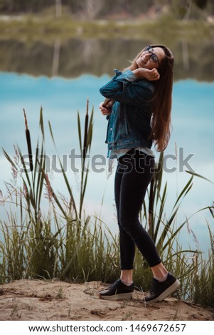 girl in jeans stands in the cattail grass on the background of the lake