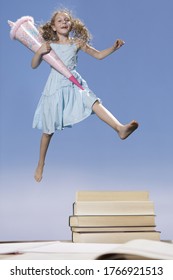 Girl jumping in air holding pink hat with books below