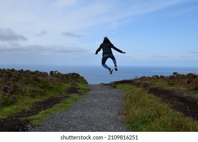 Girl jumping on a blue sky and ocean background. Green meadows. Pebble path. Hill. Panorama. Summer. Feelings. Happiness. - Powered by Shutterstock
