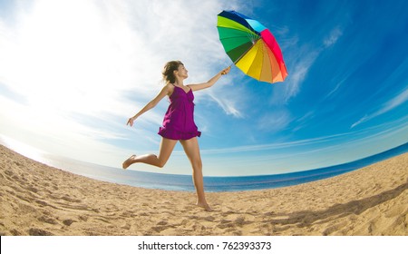 A girl is jumping with a rainbow umbrella. A woman is flying over the beach. Free flight in the wind, in the sky above the water.