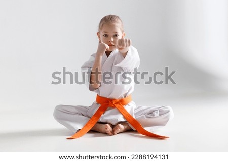 Girl karateka sits in a protective position on a white background.
