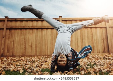 Girl, kid and playing cartwheel outdoor in backyard for autumn fun, energy and flexible in development. Person, childhood and handstand on leaves in garden with activity, game and happy in home - Powered by Shutterstock