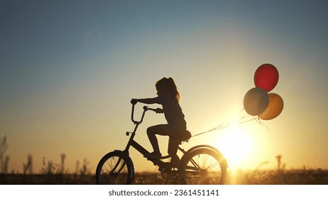 girl kid silhouette bike riding on a park. kid girl rides a bike in nature in park on the road. happy family kid dream concept. daughter plays a bike lifestyle rides on a sandy road