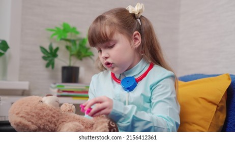Girl, kid takes care of her friend bear. Cute girl, kid of school age, plays with teddy bear toy. Child doctor combing teddy bear, childrens play at home in room. Toy patient bear, child play together