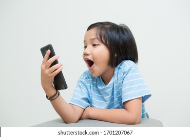 Girl Kid Using Smartphone Isolated On White Background, Looking At Mobile Phone Screen And Get Shocked With Surprise Information On Internet Or Social Network.