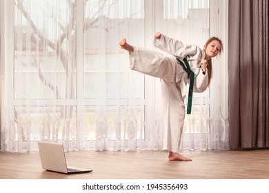 The Girl In A Kimono Stands In A Fighting Position. The Child Trains Karate At Home In Front Of A Laptop. A Taekwondo Fighter Kicks.