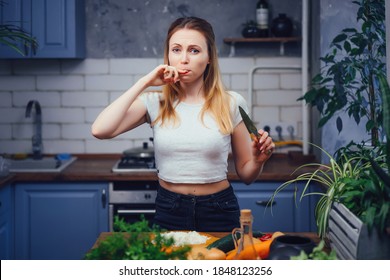 The girl in the kitchen cut her finger and licks the wound. The woman was injured while cooking. Sharp knife and safety precautions. Housewife cut herself while cutting vegetables