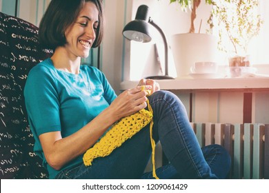 Girl Knits Crochet At Home. Woman Engaged In Needlework. A Knitter Sits On A Sofa And Works. Creative Hobby. Training Patience And Perseverance. Crochet Thick Yarn.