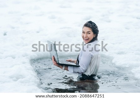 Girl with laptop in frozen lake ice hole. Woman hardening the body in cold water. Good immunity is protection against many diseases.