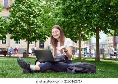 A girl with a laptop sits on the grass and talks on zoom. online work in the fresh air. - Shutterstock ID 2160162717