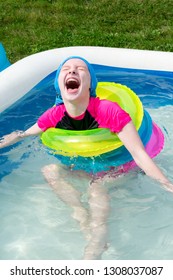 Girl Laughs In Shallow Inflatable Pool While Wearing Multiple Colorful Floats. Photo Taken In Madison, WI.