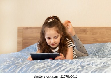 Girl Laying On Bed And Using Tablet. Watching Videos, Online Training. Quarantine. Concept Of Internet, Social Media, Online And Technology Impact To Children Life