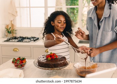 Girl learning to make cake with her mother. Girl icing cake with chocolate syrup with mom standing by at kitchen. - Powered by Shutterstock