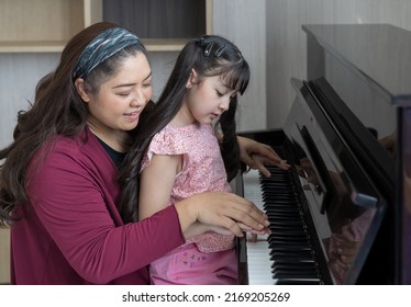 Girl Learning Piano With Teacher Woman At Home. Asian Pianist Teacher Teaching Girl Kid Student To Play Piano At School.