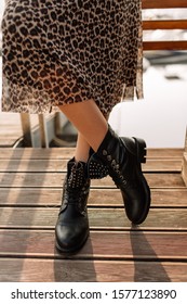Girl in a leopard skirt and black boots in hard light on a concrete floor. Light key on boots