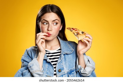 Girl Licking Her Fingers After Trying Delicious Pizza Slice, Looking At Food With Tempting Expression, Eating Out In Fastfood Pizzeria Restaurant, Yellow Background