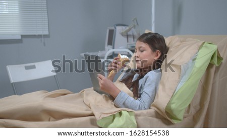 Girl lie on the bed, eat icecream and watch something on tablet