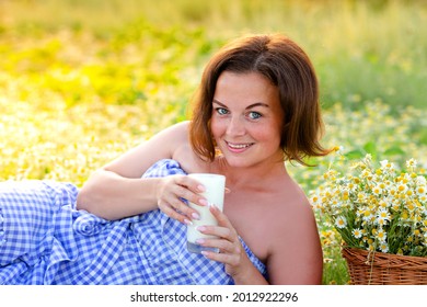 the girl lies in a chamomile field and holds a glass of milk in her hands