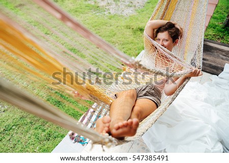 The girl lies in a hammock looking at the camera shy and modestly hides her face. Beautiful Young Woman relaxing in hammock. 