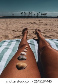 Girl lies on the beach on a towel, seashells lie on her leg. Soft focus