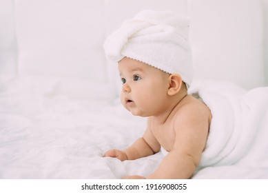 The girl lies on a white bed with a towel on her head and body. Hygiene and baby care concept. Place for text.