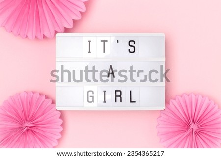 It's a girl. Lightbox with letters and tissue paper fans in a pink color. Baby shower concept. 
