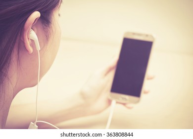 girl listening by earphone and look at smartphone in hand