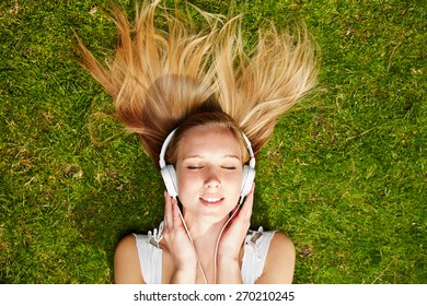 Girl listening to music streaming with headphones in summer on a meadow