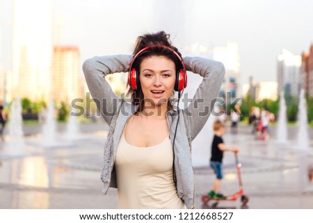 Girl listening to music streaming with headphones and dancing on the street.