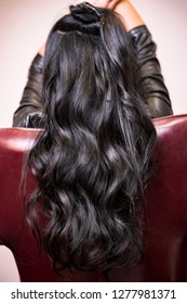 A girl with long black curly hair sits in a chair