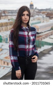 girl with long brown hair in a plaid shirt stands on a rooftop in the center of St. Petersburg