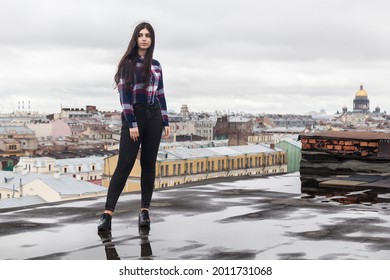 girl with long brown hair in a plaid shirt stands on a rooftop in the center of St. Petersburg