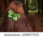 A girl with long brown hair is walking through a forest. She is wearing a green band with shamrock in her dense luxury hair. Travel and tourism in Ireland concept. Irish teenager. Park activity