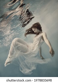     A girl with long dark hair in a white dress with glitters floats underwater as if floating in zero gravity on a light background                           
