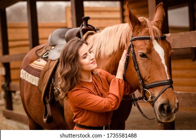 Girl in a long dress stands near a horse, a beautiful woman strokes a horse and holds the bridle. Favorite horse. The girl admires her horse. Country life and fashion, noble steed.