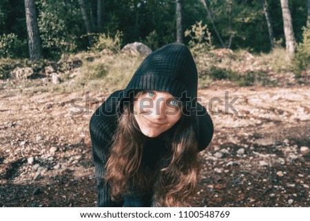 ein Mädchen mit langen Haaren und blauen Augen in den Bergen, das mit einer Kapuze lächelt