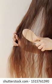 girl with long hair combing them with a wooden comb, holding strands, horizontal, close-up